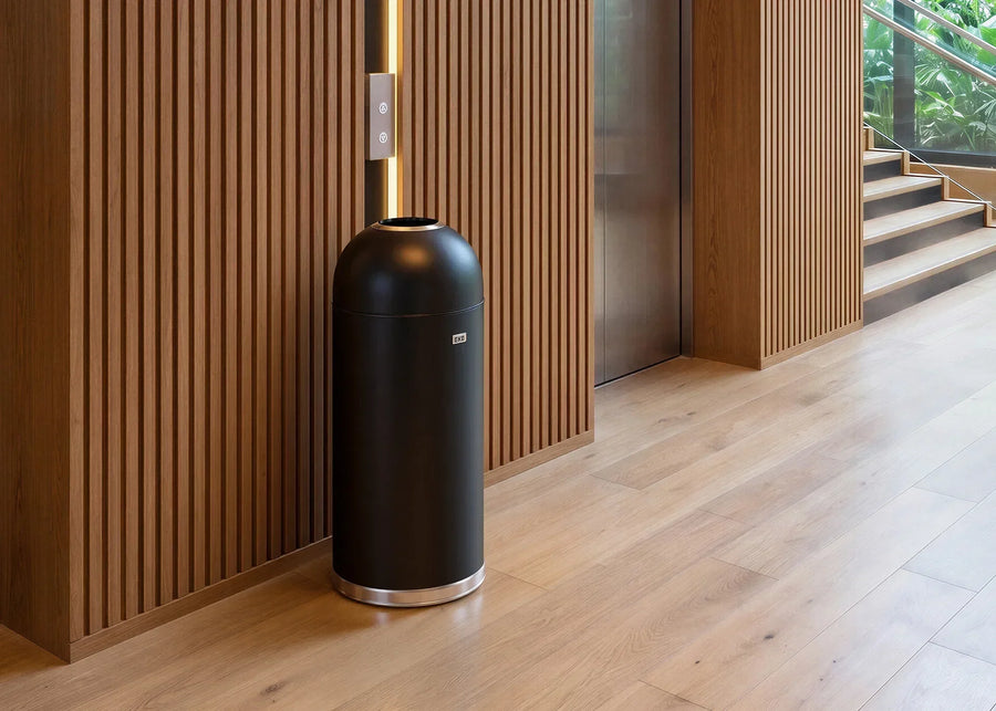 Black dome-top EKO waste bin beside an elevator in a wood-paneled hotel corridor