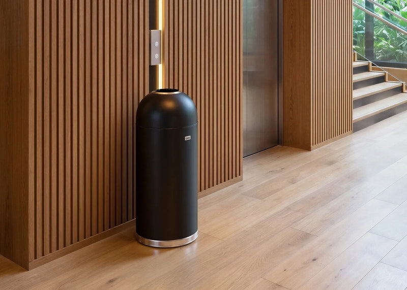 Black dome-top EKO waste bin beside an elevator in a wood-paneled hotel corridor