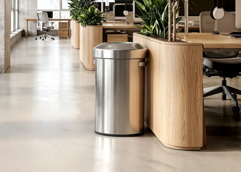 Stainless steel trash bin beside a wooden planter in a modern office workspace with natural greenery and minimalist interior design.
