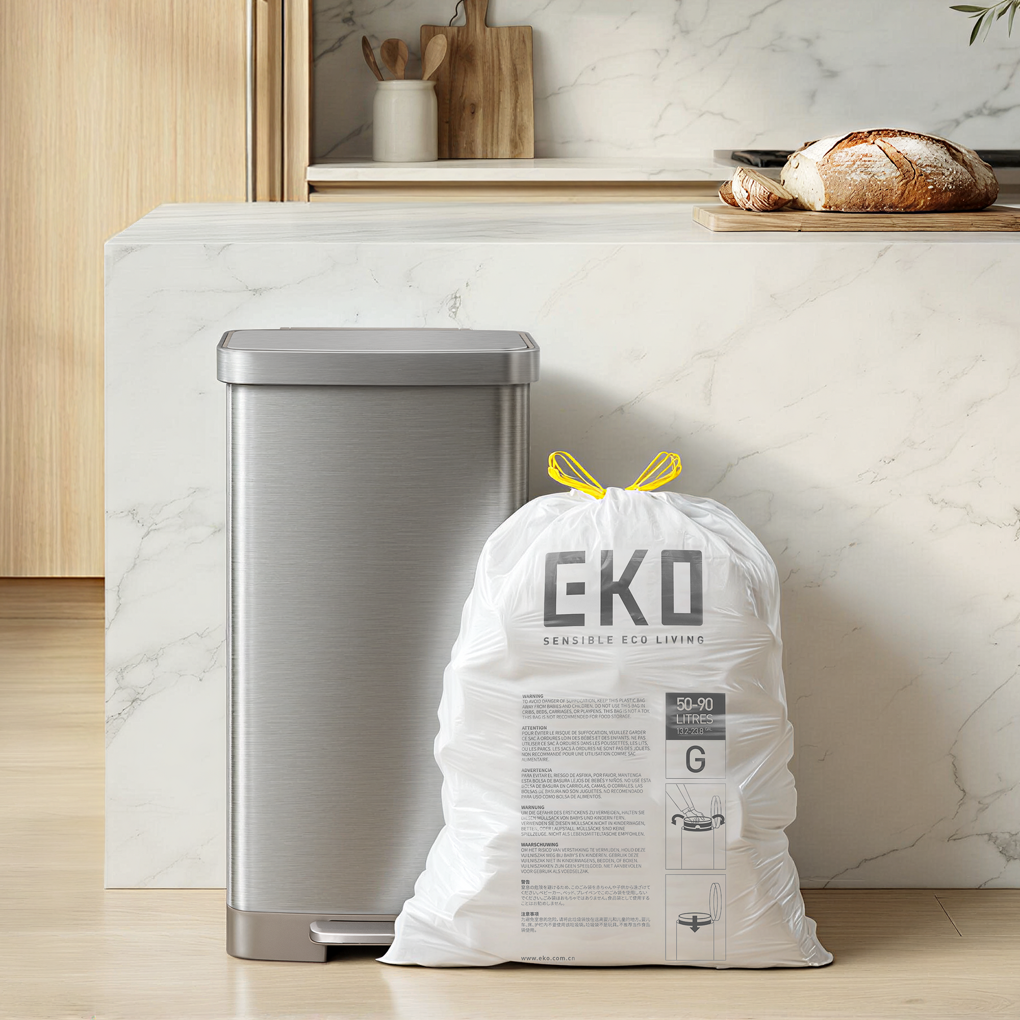 A silver mini-fridge and a large white bag labeled EKO SENSIBLE ECO LIVING stand on a marble countertop in a kitchen, near wooden items and fresh bread.