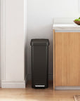 Slim EKO trash bin next to a kitchen cabinet with a bowl of fruit on a windowsill.